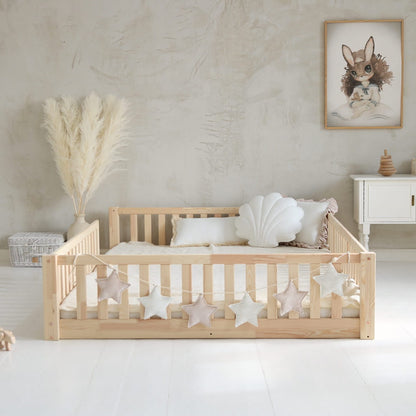 Lateral de cama montessori a ras de suelo con detalle de guirnalda en una habitación infantil.