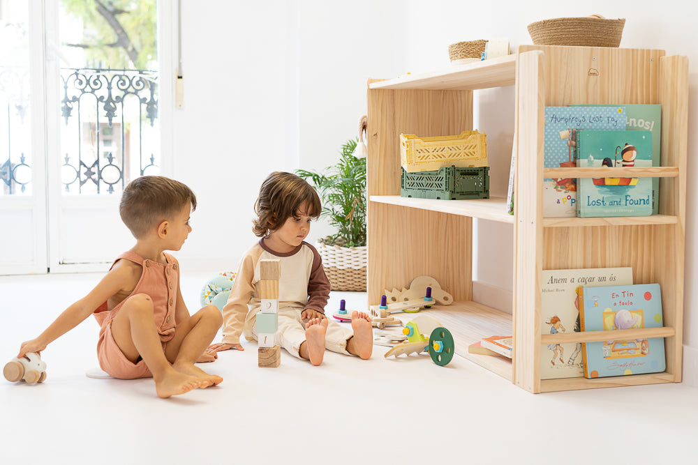 Niños en habitación infantil con la estantería Montessori con libros y juguetes organizados, fomentando la autonomía y el orden en la habitación infantil.