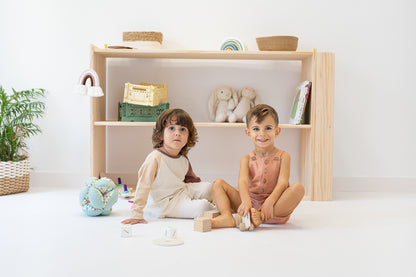 Scaffale montessoriano con libreria collocato in una stanza per bambini, a complemento della decorazione e della funzionalità dello spazio. Bambini felici che giocano.